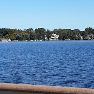 A serene view of a lake framed by lush greenery and charming houses under a clear blue sky.