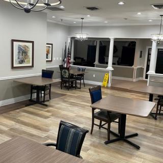 A spacious, empty room with tables and chairs, featuring flags, chandeliers, and artwork on the walls.