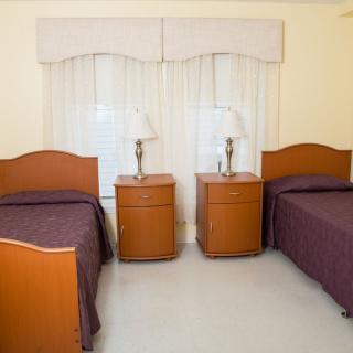 A cozy bedroom with two twin beds, each accompanied by a nightstand and lamp, set against a large window with curtains.