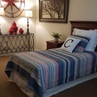 A cozy bedroom with a single bed featuring striped bedding and decorative pillows, complemented by stylish wall art and lamps.