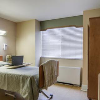 A well-lit hospital room featuring a single bed, a window with blinds, and minimalist decor.