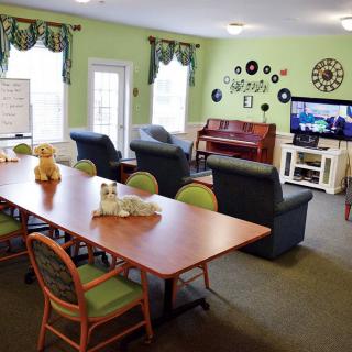 A cozy community living room with a television, piano, and various seating arrangements.