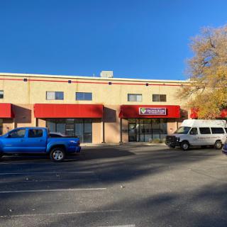 A commercial building featuring several storefronts with red awnings, accompanied by a blue truck and a white van parked in front.