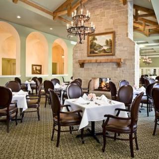 An elegant dining room with neatly arranged tables and chairs, featuring a chandelier and a fireplace.