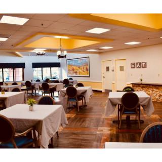 A neatly arranged dining room with tables covered in white tablecloths, surrounded by chairs and featuring warm lighting.