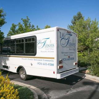 A white shuttle bus parked on a driveway surrounded by greenery and trees.