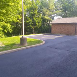 A serene parking lot surrounded by lush greenery, featuring a brick building and a lamp post.