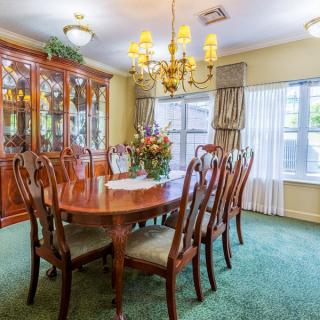 A traditional dining room with a large wooden table, elegant chandelier, and a carpeted floor.