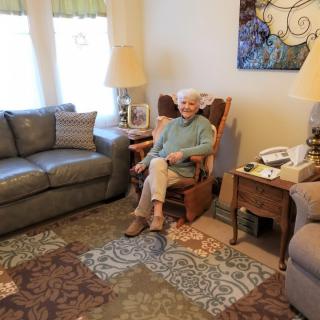 A woman sits comfortably in a living room on a rocking chair surrounded by cozy furnishings.