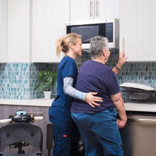 A caregiver assists an elderly person in the kitchen.