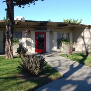 A single-story house with a red door, surrounded by neatly maintained landscaping on a sunny day.