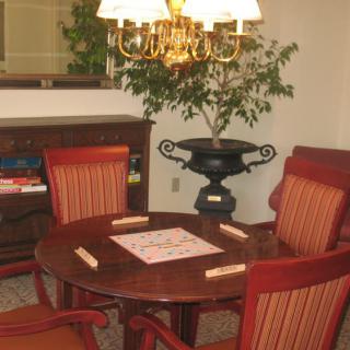 A cozy room with a table set for a board game, surrounded by chairs and illuminated by an overhead lamp.