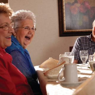 A group of seniors enjoying a joyful moment together at a dining table.