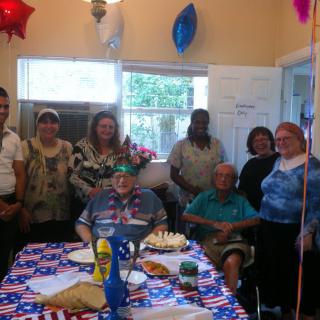 A group of people gathered around a table decorated with a patriotic theme, celebrating an event indoors.