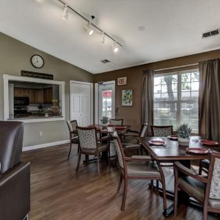 A cozy dining area with wooden tables and chairs, featuring large windows and elegant curtains.