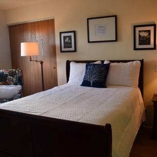 A cozy bedroom featuring a neatly made bed, artwork on the walls, and a standing lamp.