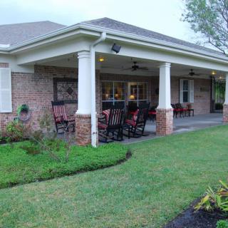 A brick building with a covered patio and outdoor seating, surrounded by a well-maintained lawn.