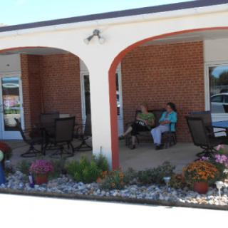 A serene outdoor seating area in front of a brick building, featuring women enjoying a leisurely moment amidst colorful flowers.