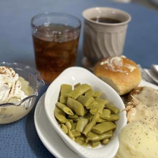 A comforting home-cooked meal featuring green beans, a roll, and dessert accompanied by tea and coffee.