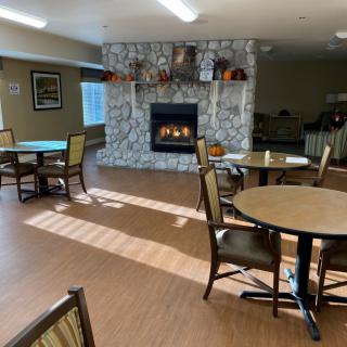 A cozy dining area with tables and chairs arranged around a fireplace.