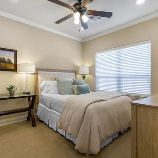 A cozy bedroom interior featuring a neatly made bed, soft lighting, and a ceiling fan.