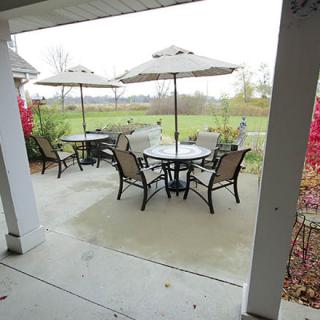 A cozy patio setup with outdoor tables, chairs, and umbrellas overlooking a garden.
