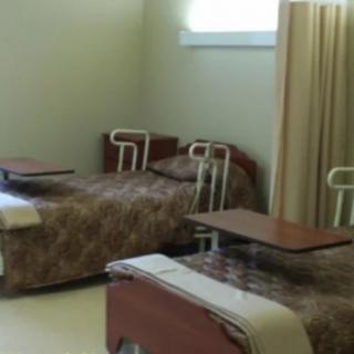 A hospital room with two beds equipped with adjustable tables and privacy curtains.