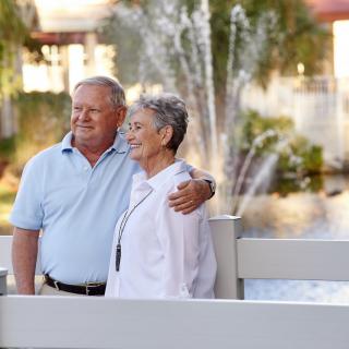 An elderly couple enjoys a sunny day by the fountain in a park.