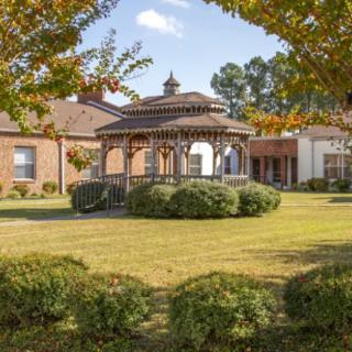 A scenic view of a garden with a wooden gazebo surrounded by trees and shrubs.