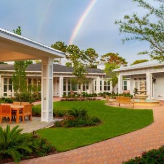 A serene outdoor space featuring contemporary architecture, lush greenery, and a vibrant rainbow in the background.