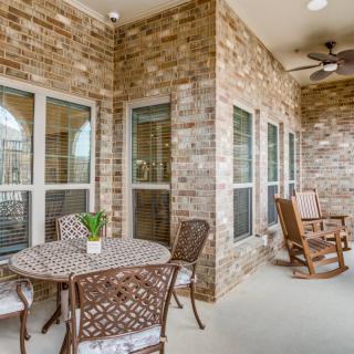 A cozy patio with brick walls featuring a table and chairs, along with rocking chairs under a ceiling fan.