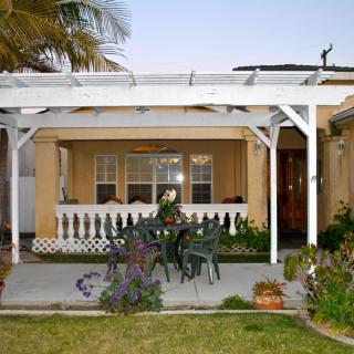 A cozy backyard patio with a pergola and outdoor seating surrounded by plants.
