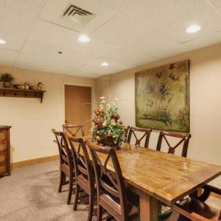 A cozy dining room with a long wooden table surrounded by chairs and decorated with artwork and floral arrangements.