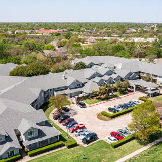 Aerial view of a residential building complex with a parking lot and surrounding greenery.