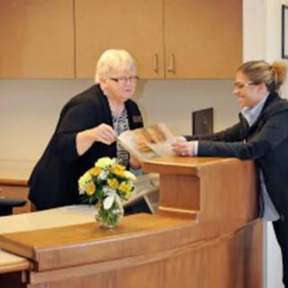 Two people interacting at a reception desk in an office setting.