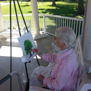 An elderly person painting outdoors on a sunny day.