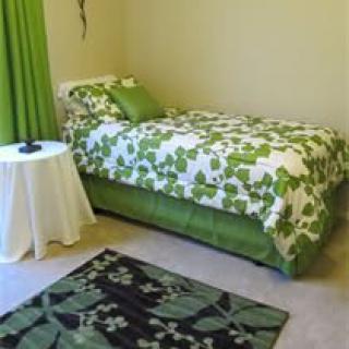 A bedroom with a green and white floral bedspread, matching curtains, and a decorative rug.