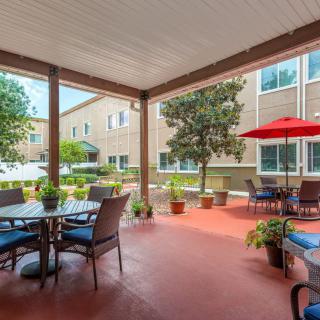 A cozy patio area with outdoor seating, surrounded by lush plants and a red umbrella.