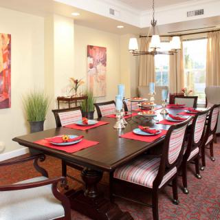 An elegant dining room with a large table set for a meal, surrounded by chairs and illuminated by a chandelier.