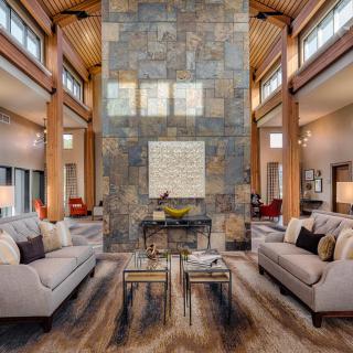 A luxurious, modern living room featuring high ceilings and a central stone wall with elegant furniture and wood beams.