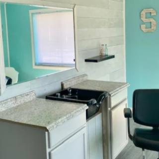 A compact kitchenette with a stovetop, sink, and chair in a small room.