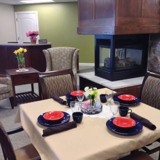 A cozy dining area with a neatly set table, featuring colorful plates and flowers, beside a modern fireplace.