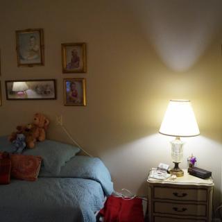 A cozy bedroom with a bed, nightstand and lamp, decorated with pictures on the wall.