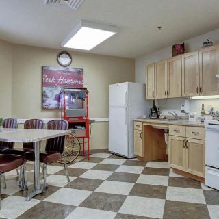 A cozy kitchen and dining area featuring a refrigerator, table with chairs, wooden cabinets, and a popcorn machine on a checkered tile floor.