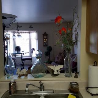 View from the kitchen sink, reflecting a dining area through the mirror with flowers and bottles on the counter.