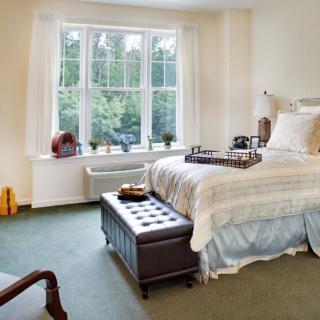 A cozy bedroom with a large window, neatly decorated with comfortable furnishings.