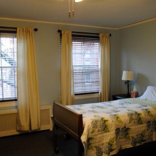 A cozy bedroom with a single bed, two windows with curtains, and a bedside lamp.