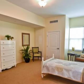 A cozy bedroom with simple decor, featuring a bed, dresser, chair, and indoor plants.