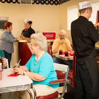 A retro-style diner where people enjoy their meals and a waiter attends to customers.