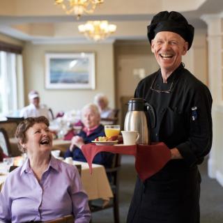 A cheerful server in a dining room bringing coffee to an elderly group, creating a warm and friendly atmosphere.